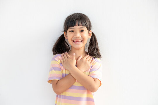 Close up of cute happy small girl isolated on white background hold hands at heart chest feel grateful, smiling little child with eyes closed pray thanking god high powers, faith concept