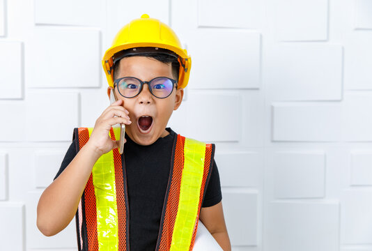 Young Asian boy wearing glasses, black shirt, yellow safety vest and helmet standing near white wall and shout out loud as shocked or exciting on unexpected contacting info from smartphone calling
