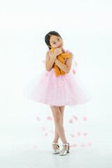 Portrait isolated studio shot of little Asian cute ballerina kid in pink beautiful elegance rose flower ballet dress standing hugging orange fluffy teddy bear doll in arms in front white background