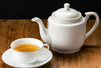 View of white ceramic cup of hot tea and tea kettle on wooden table.