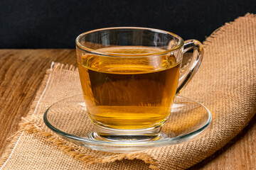 Side view of a cup of hot tea in saucer on sack cloth. Hot tea in a transparent glass on sack cloth.