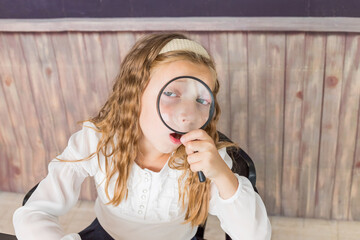 education and school concept - little girl with magnifier at school. schoolgirl sitting in the classroom. Child in an elementary school. Education and learning for kids.