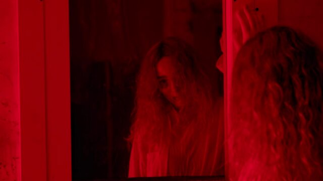 Woman in straitjacket standing in front of a mirror and seeing a screaming man behind it