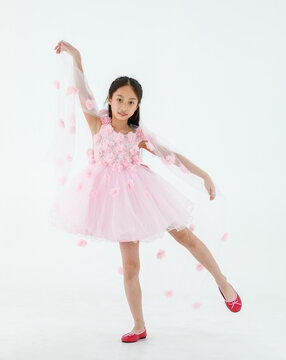 Isolated full body studio shot of little cute pretty Asian ballerina kid wears pink beautiful roses flowers ballet dress and red shoes smiling posing dancing happily in front of white background