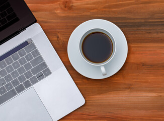 Top view shot of laptop notebook computer with black coffee in white ceramic cup on wood background with copy space