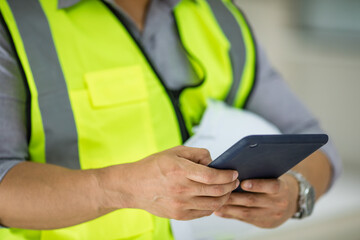 Handsome young Asian engineer in yellow reflective vest using tablet computer