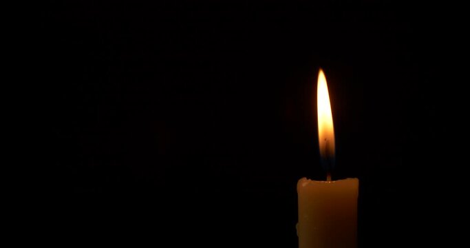 Close-up burning single candle flame isolated on black background, 4K video