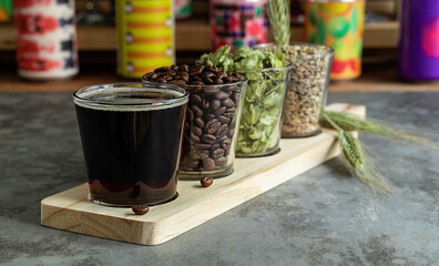 Wooden board for flight set craft beer tasting. Coffee stout or porter with ingredients. Bar with different cans in the blurred background. 