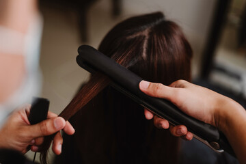 Hair salon concept a male hairstylist working with a hair straightener to straighten a female...