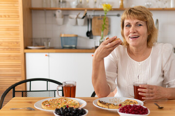 A middle-aged woman eats pizza in the kitchen.