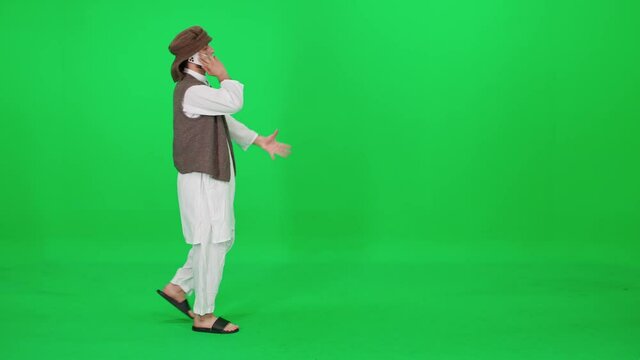 A man of Arab appearance in traditional clothes walking and talking on a mobile phone against the background of a chromakey.