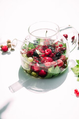 Tea with summer berries in a transparent teapot