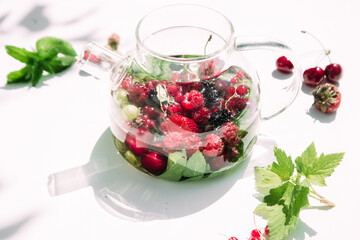 Tea with summer berries in a transparent teapot