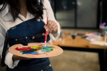 Fototapeta premium Cropped shot female artist mixing color on palette while painting picture in art studio.