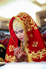 Portrait of young and beautiful Asian bride wearing traditional dress sitting with hands praying gesture and eyes closed in Minangkabau muslim tradition culture wedding ceremony.