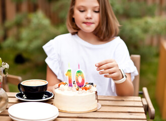 Happy adorable girl with birthday cake in cafe terrace. 10 year old celebrate birthday.