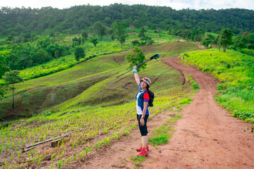 Obraz premium Asian female trail runner wearing sportswear is taking a portrait with a view of a high mountain running track in a dirt road on a clear day, with a mountain view in the background.
