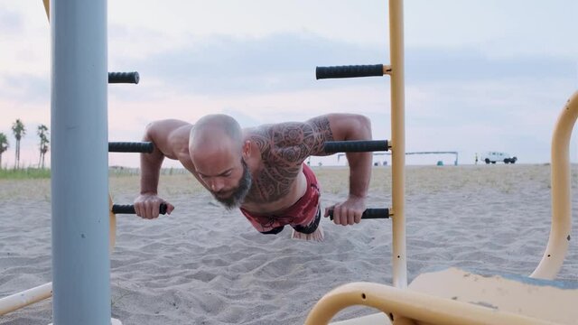 Athlete man doing push up with parallel bars in a calisthenics park at the beach. Sport, strength and motivation concept.
