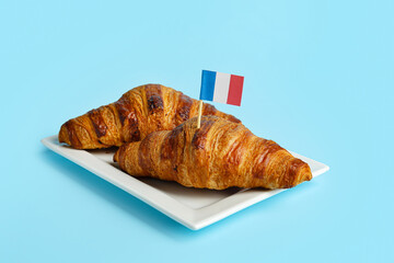 Plate with tasty croissants and flag of France on color background