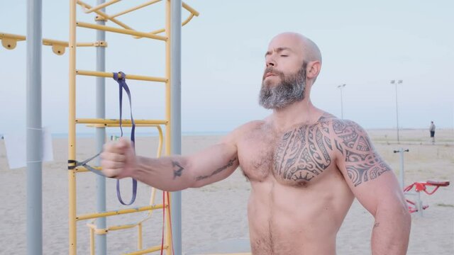 Fitness man doing calisthenics chest workout with a resistance rubber band at the beach. Sport concept.