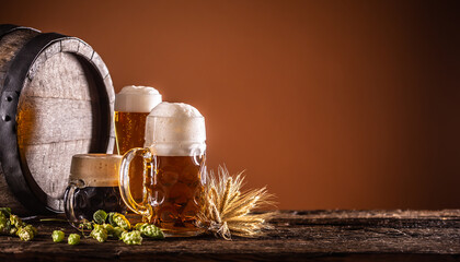 Three glasses with draft beer in front of a wooden barrel. Decoration of barley ears and fresh hops