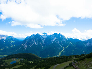 Fototapeta na wymiar Panoramic view from Grubigstein, with rugged Zugspitze in background under blue sunny sky with cumulus clouds. Green valley at the foot of majestic alpine mountains, in Lermoos, Tyrol
