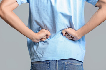 Young man suffering from back pain on grey background