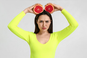 Upset young woman with grapefruit on light background