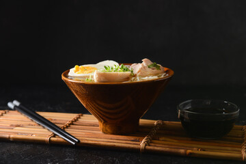 Tasty Chinese soup with chicken in bowl with soy sauce on dark background