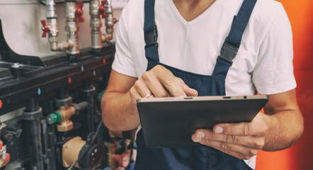 The technician checking the heating system in the boiler room with tablet in hand