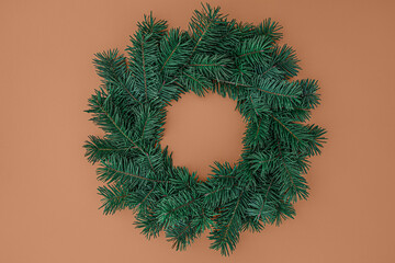 Retro Christmas brown backdrop. Festive winter Xmas wreath made of green fir tree branches on beige background. Trendy minimal xmas ornament template. Top view, flat lay, copy space. 