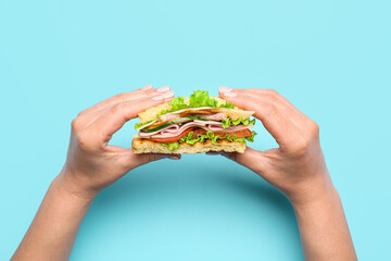 Female hands with tasty sandwich on color background