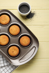 Baking tin with delicious muffins and bowl with poppy seeds on color wooden background