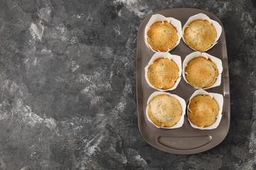 Baking tin with delicious poppy seed muffins on dark background