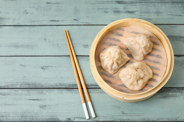 Bamboo steamer with tasty dumplings and chopsticks on color wooden background