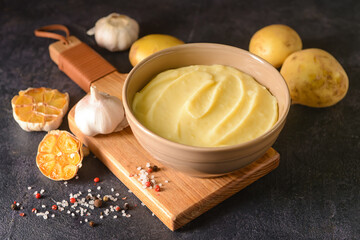 Bowl of tasty mashed potatoes with garlic and vegetables on dark background