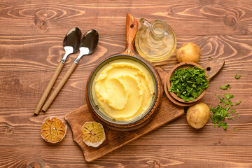 Bowl of tasty mashed potatoes with garlic and ingredients on wooden background