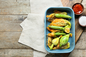 Baking dish with fried zucchini flowers, sauce and salt on wooden background