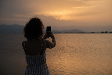 Woman using her mobile phone to takes photos to the sunset.