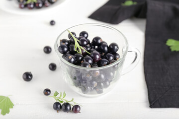 Glass cup with ripe black currant on light wooden background