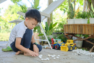 Cute Asian young kindergarten boy playing with pebbles and toy construction machinery, Happy smiling kid playing alone at home backyard , Montessori education, Creative play for kids