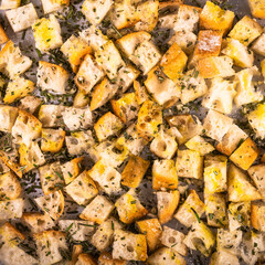 Cooking croutons - sliced ciabatta bread with olive oil and rosemary on a baking sheet, top view, close-up
