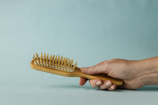 A wooden hairbrush with hair in womans habd on light blue backgraound with copy space