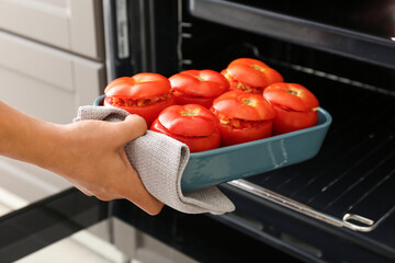 Woman putting baking dish with uncooked stuffed tomatoes in oven, closeup