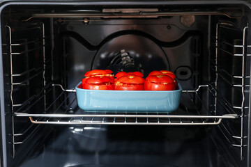 Baking dish with uncooked stuffed tomatoes in oven