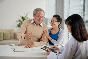 Fototapeta premium Senior couple telling preferences and expectations of new house to real estate agent who is filling document on tablet computer