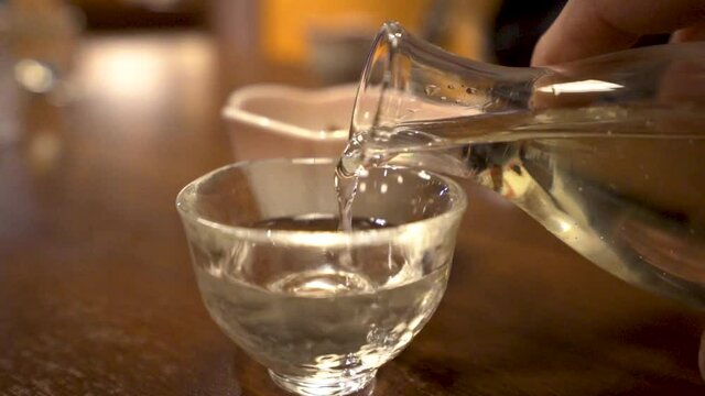SLOWMO close up of man's hand pouring sake into a cup