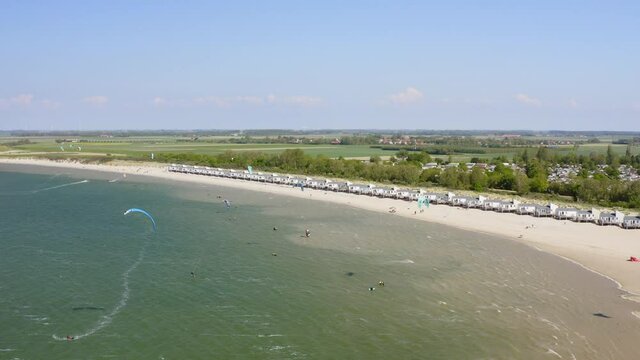 Aerial backward establishing shot of a group of kitesurfers practicing by the beach on a windy day near Wissenkerke, the Netherlands