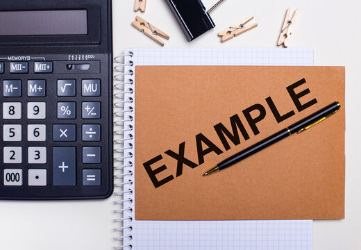 On the desktop is a calculator, a pen and clothespins near a notebook with the text EXAMPLE. Business concept. View from above