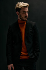 stylish man with a fashionable hairstyle and in a leather jacket orange sweater black background
